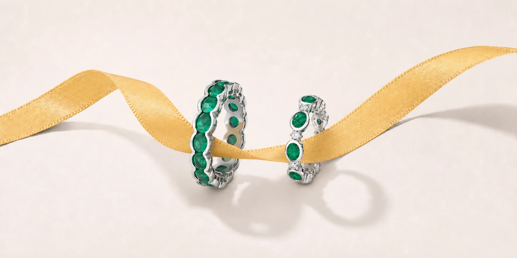Two green gemstone rings arranged across a golden ribbon